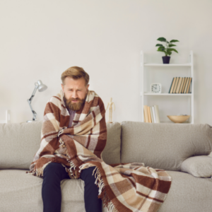 Person sitting on their couch wrapped in a blanket, looking cold.