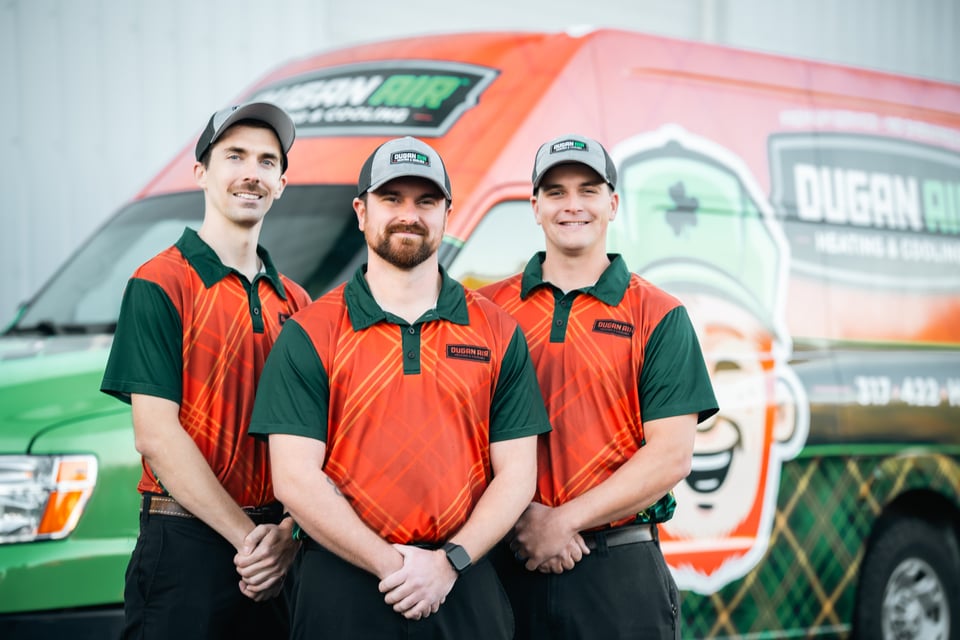 Three HVAC technicians in matching Dugan Air uniforms stand in front of a branded company van