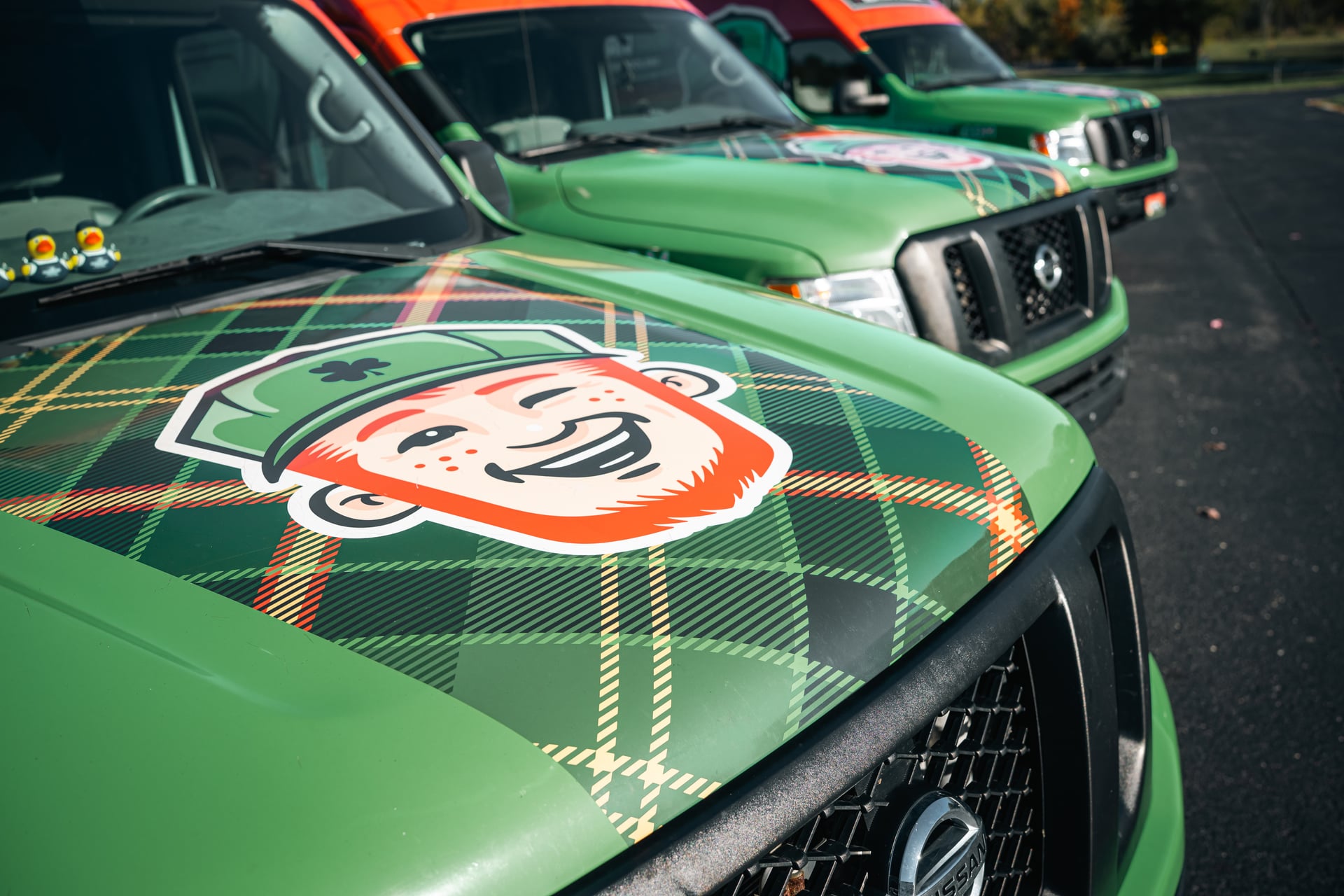 Green trucks parked in a row in Franklin IN, each with a plaid pattern and the cartoon face of a smiling red-headed character in a green cap on the hood—perfectly representing local ductwork services.