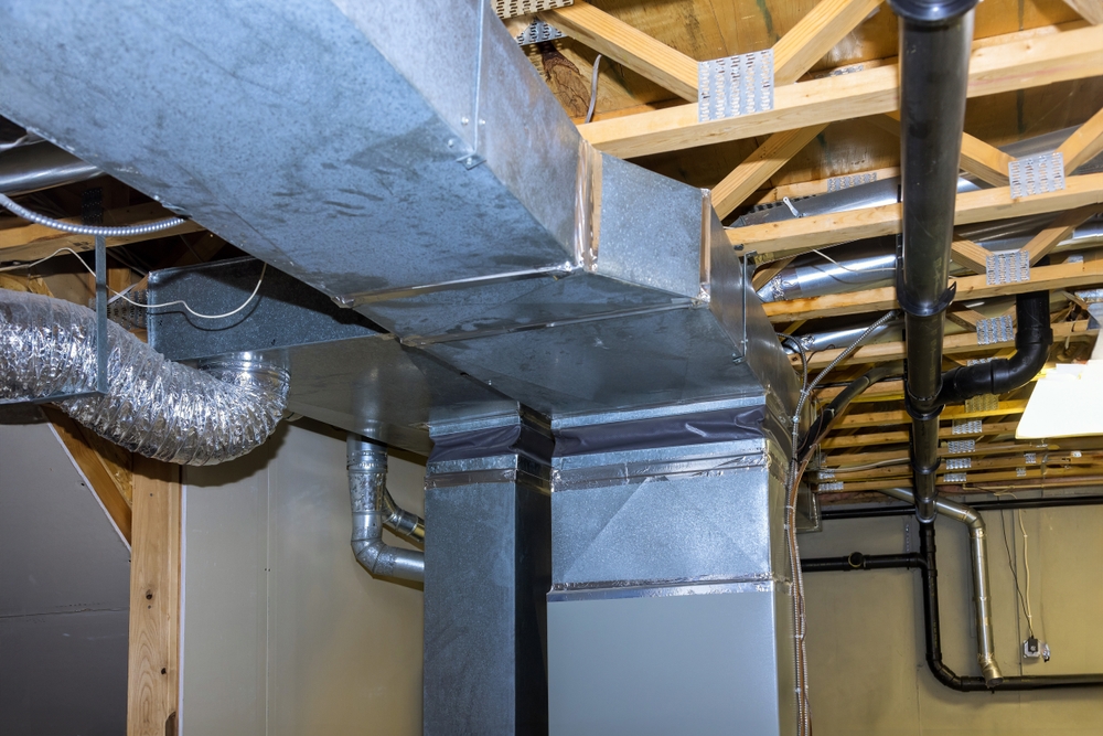 Exposed HVAC ductwork, pipes, and wooden ceiling beams are visible in an unfinished basement or utility area—ideal for those in Franklin IN seeking professional ductwork services.